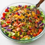 A colorful bowl of Cowboy Salad with black beans, corn, and avocado on a wooden table.
