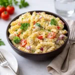 A colorful bowl of Creamy High Protein Pasta Salad on a sunny wooden table