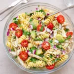 Healthy chicken pasta salad with avocado in a white bowl on a wooden table.