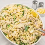 A large bowl of creamy Lemon Pasta Salad with chicken and arugula on a wooden table.