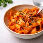 A vibrant raw carrot salad with ribbons and parsley in a white bowl.