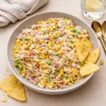 A bowl of Viral Tuna Salad with jalapeño chips and peas on a wooden table