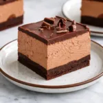 A stack of triple-layer Chocolate Mousse Brownies on a wooden board.